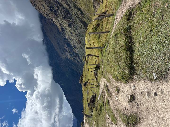 Undulating path lined by rustic wooden posts leads toward cloud-shrouded Andean mountains