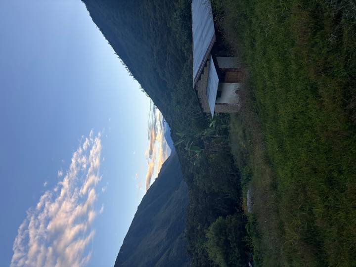 Twilight view down a lush green valley toward distant snow-capped peaks with a rustic hut in foreground