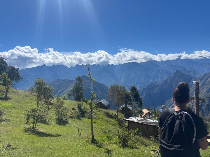 Hiker looks over dramatic layers of Andean ridges under billowing clouds from a grassy hillside