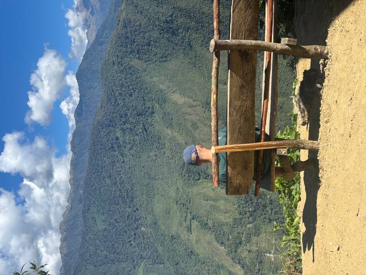 Man sits on a rustic bench at a scenic overlook with sweeping green valleys below and a dog resting underneath