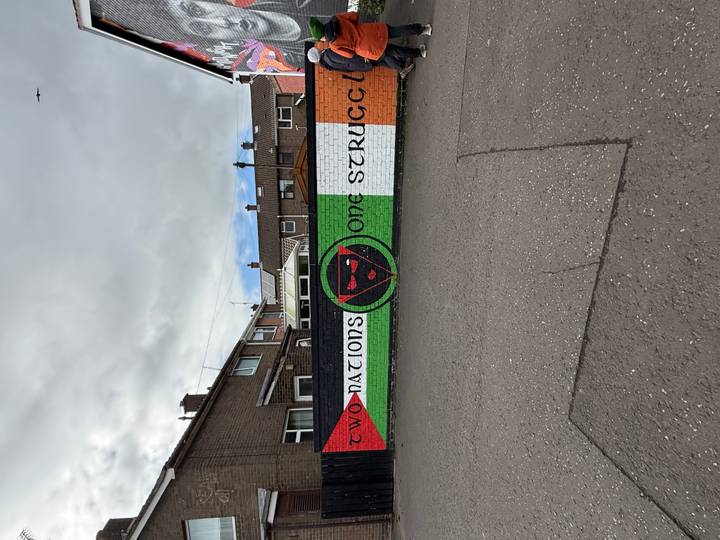 A politically charged street mural reads 'Two Nations One Struggle' on a brick wall.
