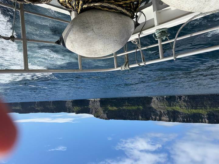 View of towering sea cliffs from the deck of a boat with a finger slightly obscuring the lens.