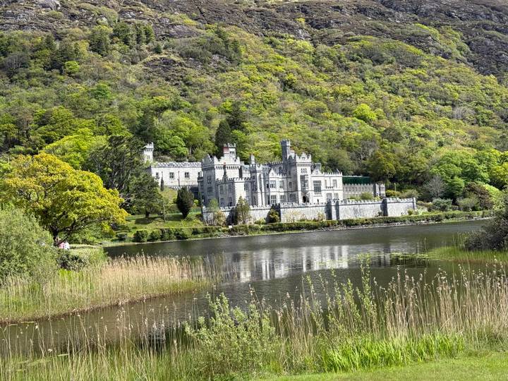 Kylemore Abbey's grey neo-Gothic walls reflect in a calm lake framed by fresh spring foliage.