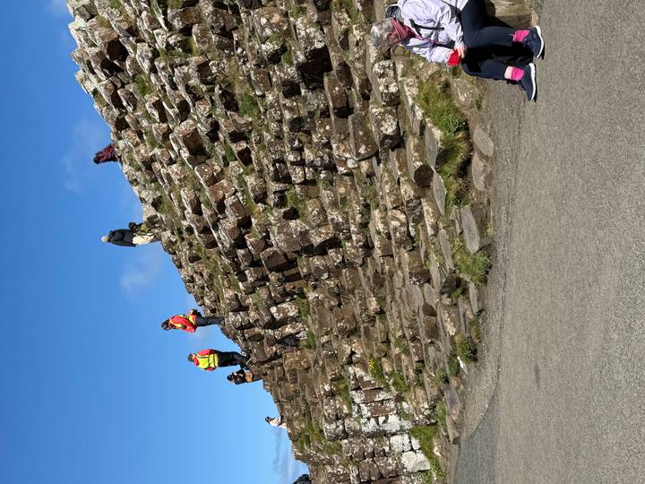 Visitors explore the hexagonal basalt steps of the Giant's Causeway slope on a sunny day.