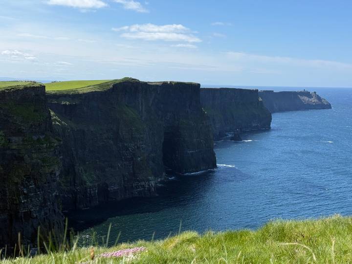 The sheer vertical walls of the Cliffs of Moher loom over the Atlantic Ocean in bright light.