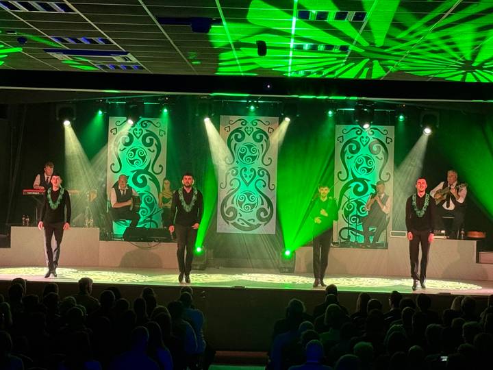 An energetic Irish dance performance unfolds on stage under vivid green lighting.