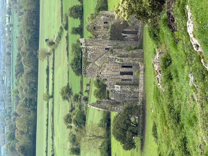 Ancient stone ruins sit amid patchwork green farmland stretching into the distance.