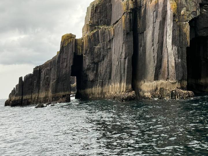 Jagged basalt sea caves and pillars rise from dark waters under a moody sky.