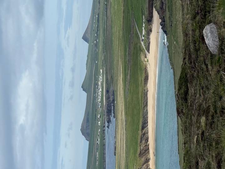Rolling green peninsulas and sandy beaches are seen beneath distant pointed mountains.