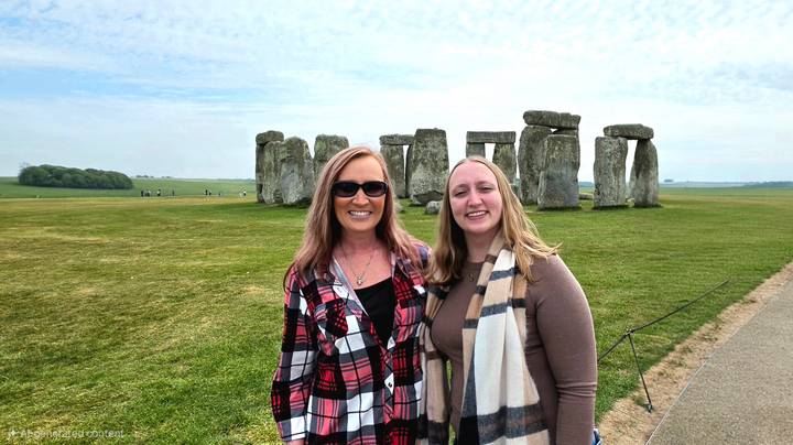 Travellers pose before the ancient stone circle of Stonehenge surrounded by open grassy plain and blue sky.