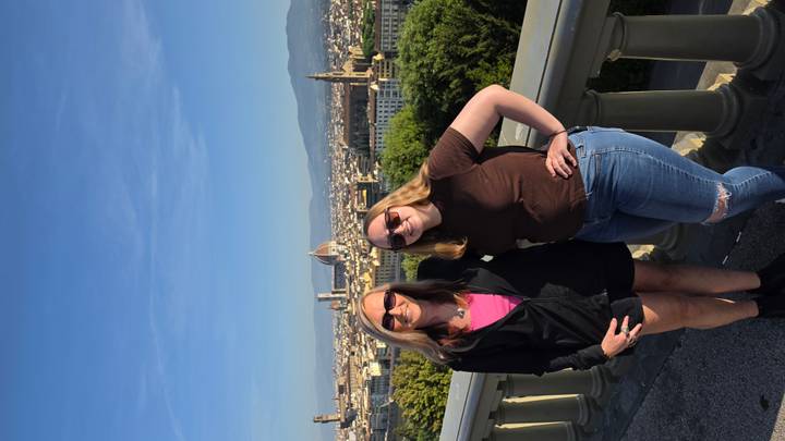 Two women overlooking the skyline of Florence with the Duomo and Tuscan hills under a clear blue sky.