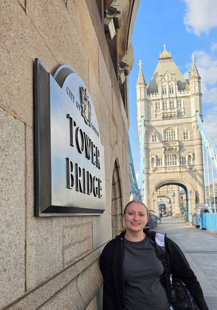 Close-up of Tower Bridge name plaque with the iconic bridge tower rising in soft focus behind a traveller.