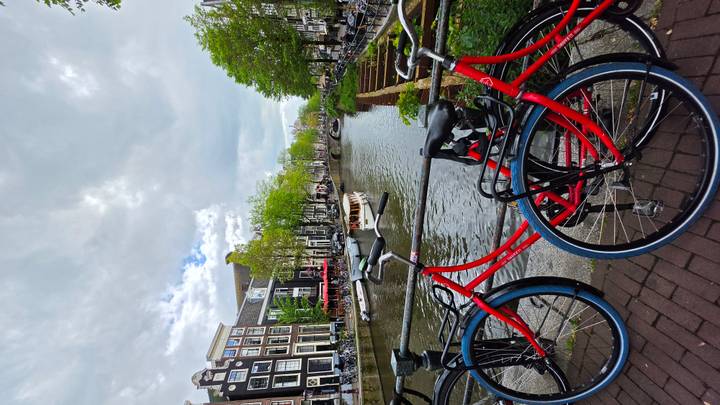 Amsterdam canal lined with historic gabled houses and red rental bikes in the foreground under dramatic clouds.