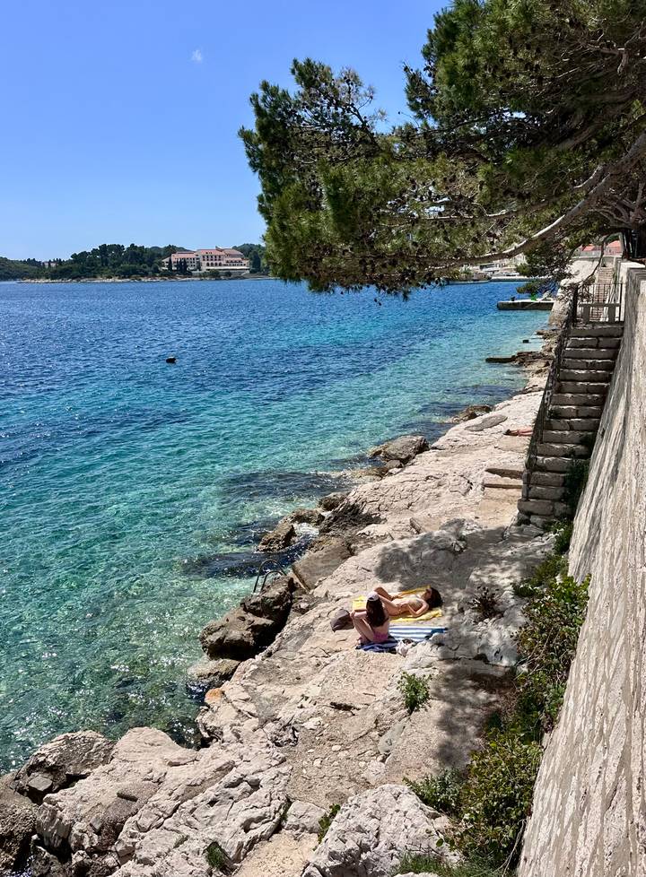 A sunbather relaxes on rocky steps beside crystal-clear Adriatic waters.