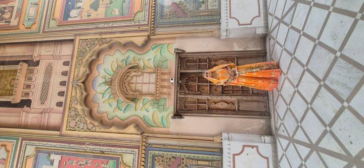 Woman in vibrant Rajasthani attire poses before an ornate carved doorway and painted arch in an Indian palace.