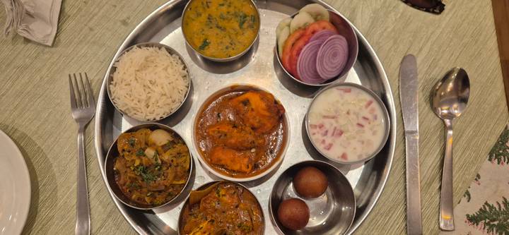 Traditional Indian thali platter featuring curries, rice, breads, sweets and fresh vegetables on a metal tray.