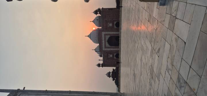 Silhouetted Mughal mosque within the Taj Mahal complex at sunrise with soft pastel sky.