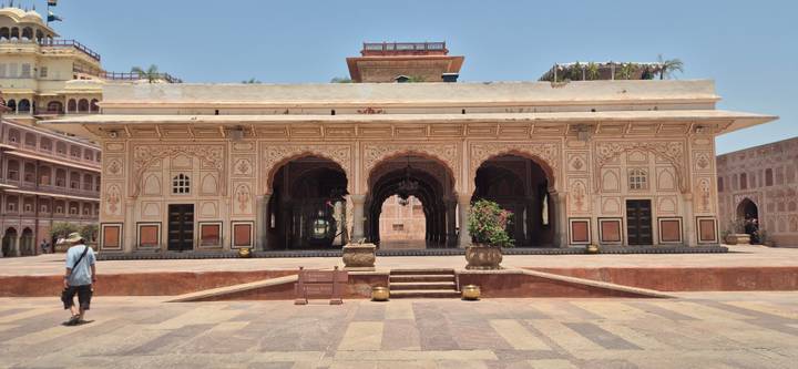 Intricately painted pavilion with arched entrances in an Indian palace courtyard under bright midday sun.
