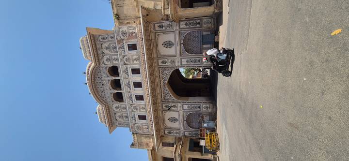 Motorcyclist passes beneath an ornate historic gate with detailed frescoes and lattice windows.