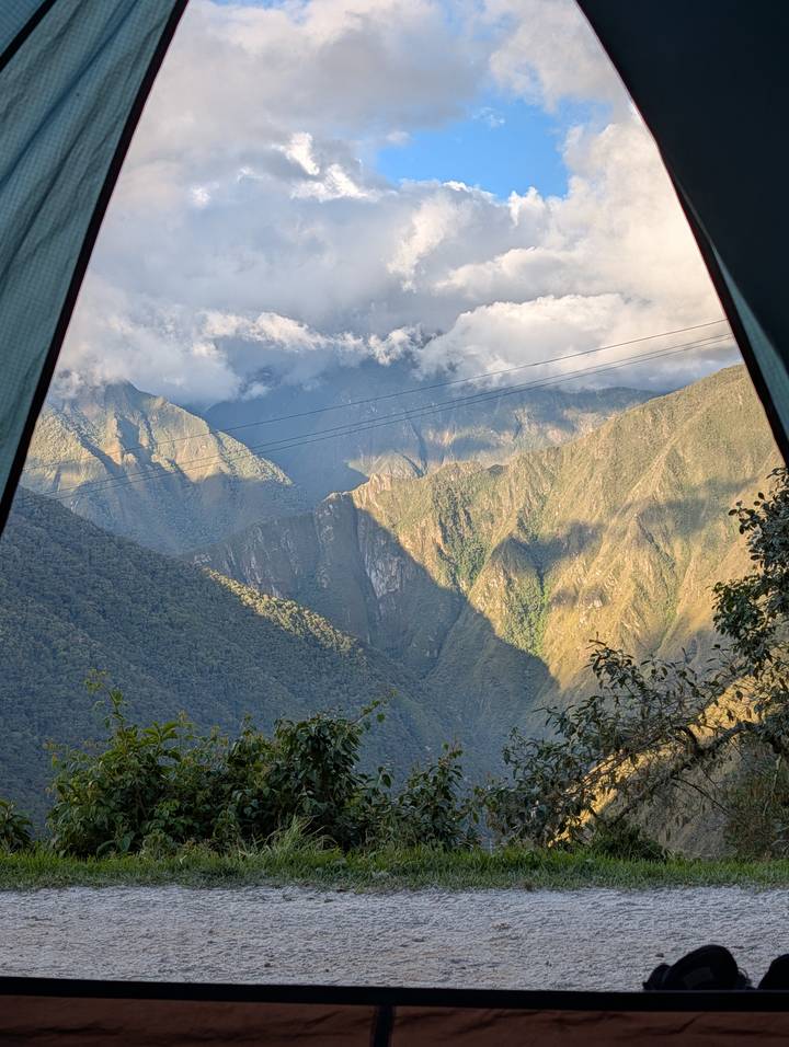 Mountain vista framed by open tent flaps with dappled sunlight and distant clouds.