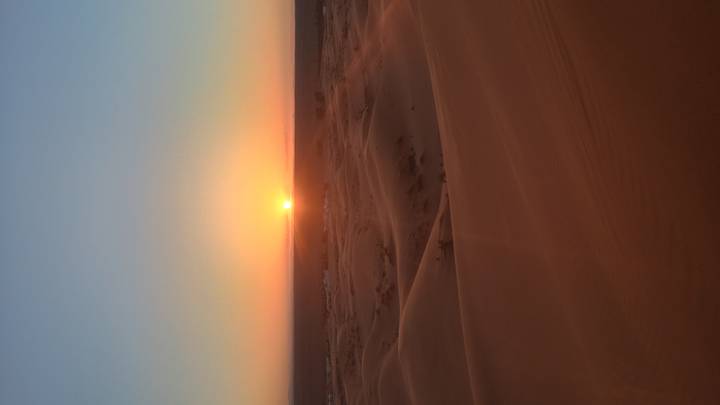 Golden sun sinks below endless Sahara dunes casting warm light over rippled sand.