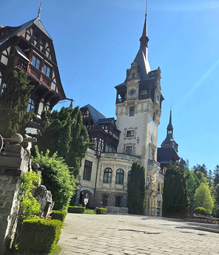 Neo-Renaissance Peles Castle rises amid evergreen forests under a bright Carpathian sky.