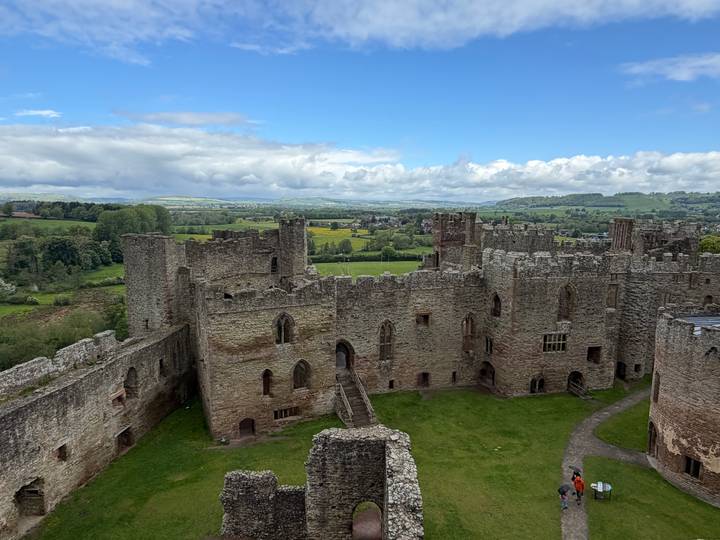 Stone walls and towers of Ludlow Castle seen from a higher viewpoint against blue skies