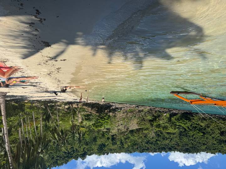 Secluded tropical beach with clear turquoise water, people relaxing on the sand and a banca boat offshore