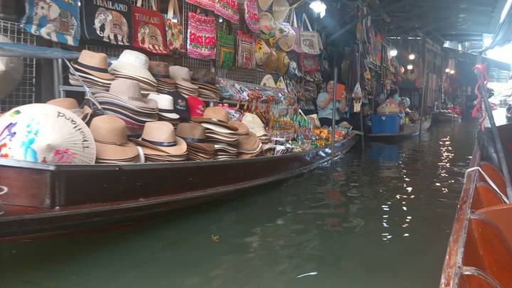 Merchandise-laden boat selling hats and souvenirs drifting through a covered floating market alley.