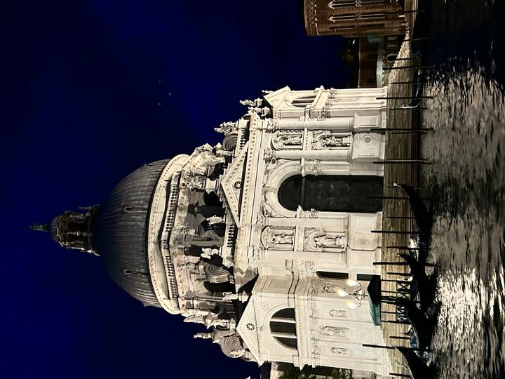 Santa Maria della Salute basilica illuminated at night with gondola posts in foreground.