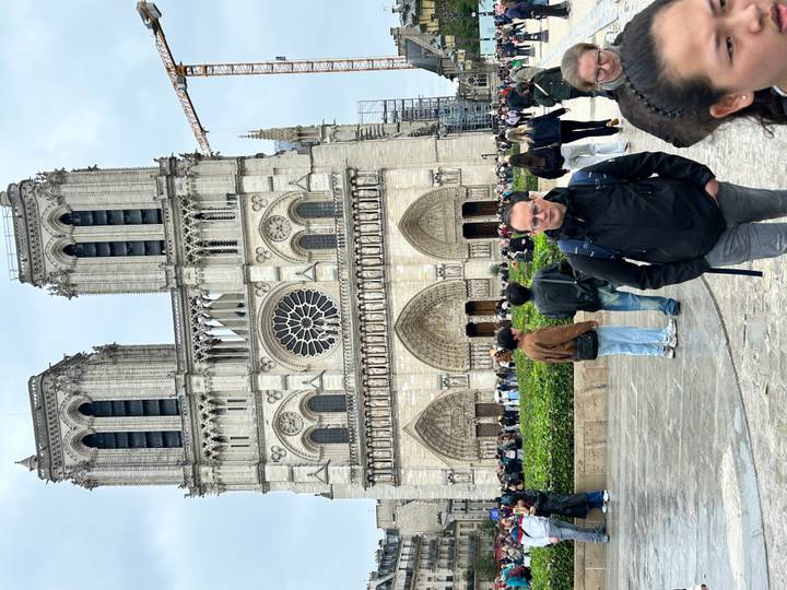 Crowds in front of Notre-Dame Cathedral facade with rose window on cloudy day.