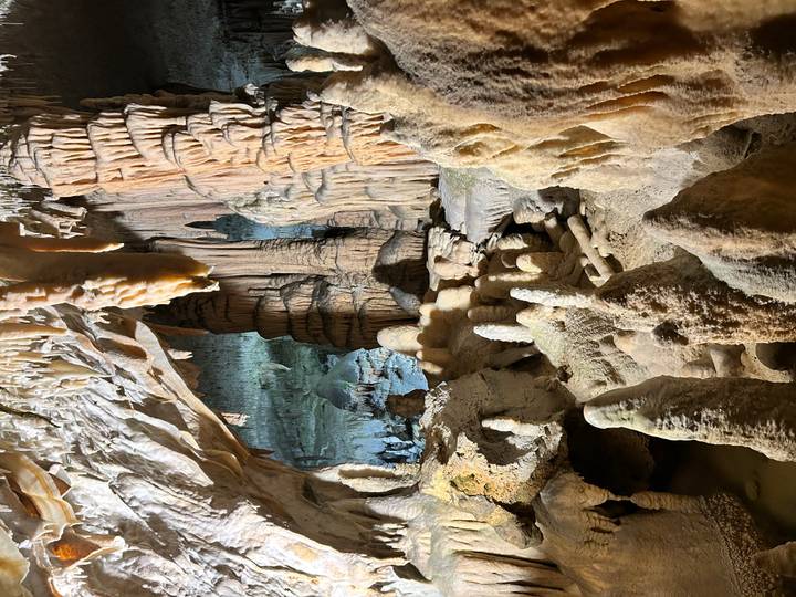 Dramatic limestone cave interior with stalactites and stalagmites lit by warm lights.