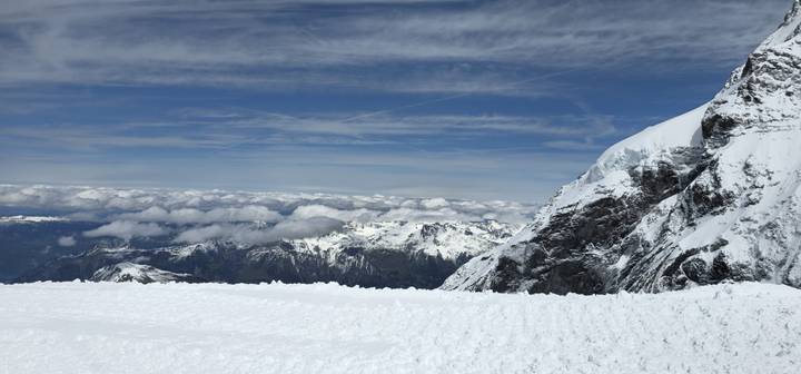 Snow-covered alpine plateau with Jagged peaks and a sea of clouds below, Swiss Alps.
