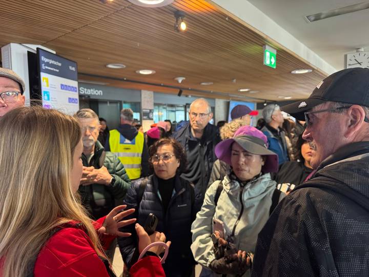Travellers listen to a guide inside a busy alpine train station terminal.