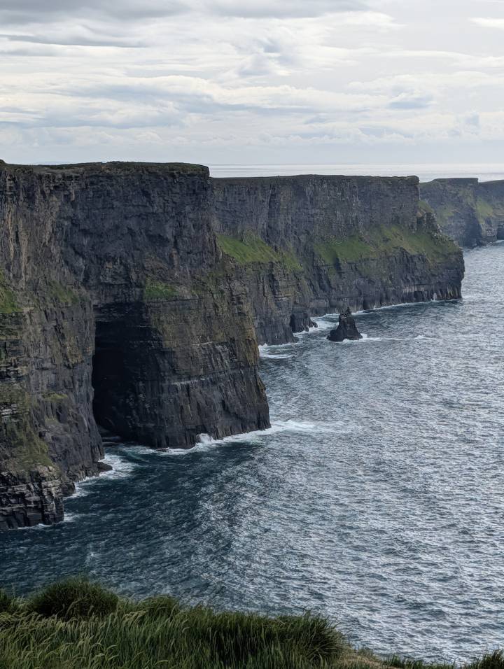 Dramatic sheer sea cliffs with dark rock faces rise above choppy Atlantic waters.