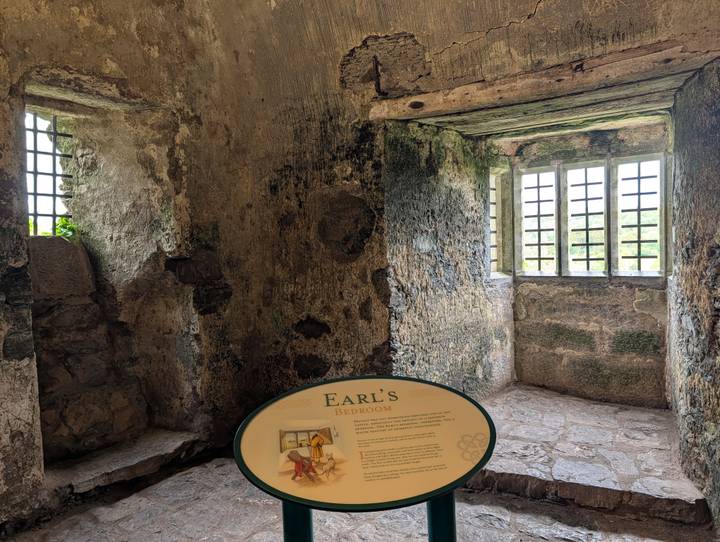 Stone room inside castle with barred windows and an informational sign titled 'Earl's Bedroom'.