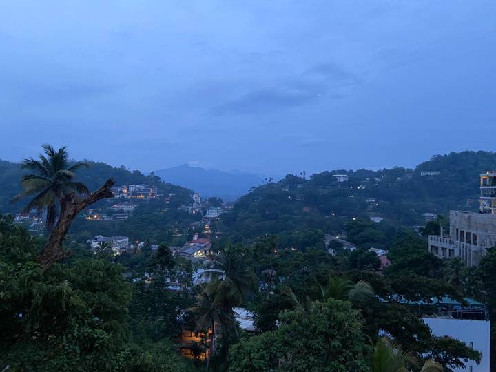 Blue hour panoramic view over Kandy valley with twinkling lights among treetops and hills.