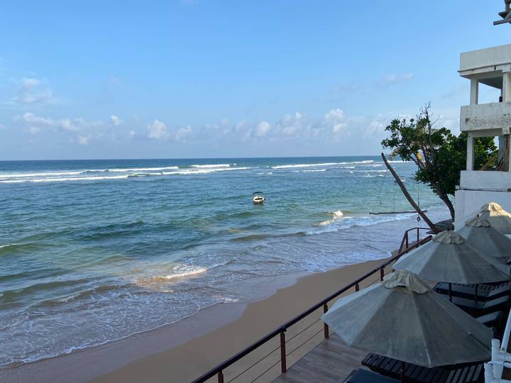 Peaceful sandy beach with small waves and a lone boat viewed from a seaside balcony.