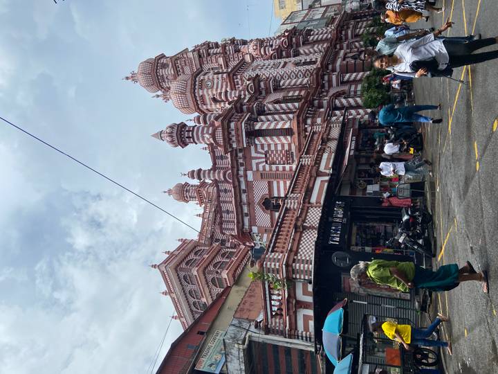Red-and-white striped mosque façade with street activity in front under cloudy sky