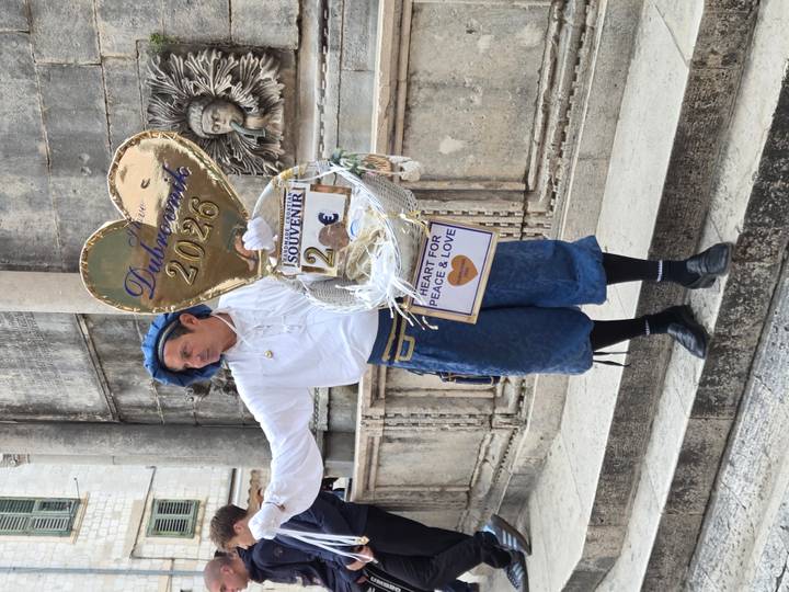 Costumed street performer in Dubrovnik holding heart-shaped souvenir sign