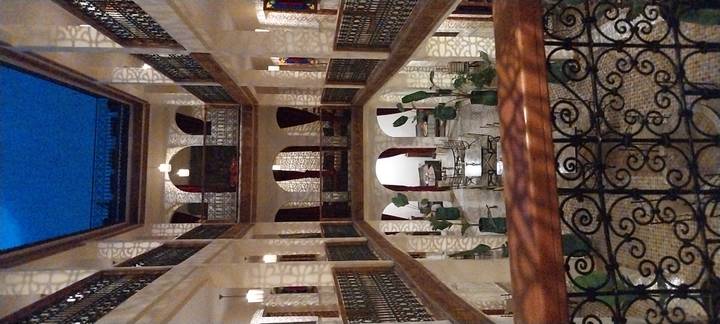 An ornate multi-storey riad interior with patterned tiles, arches and soft evening lighting.
