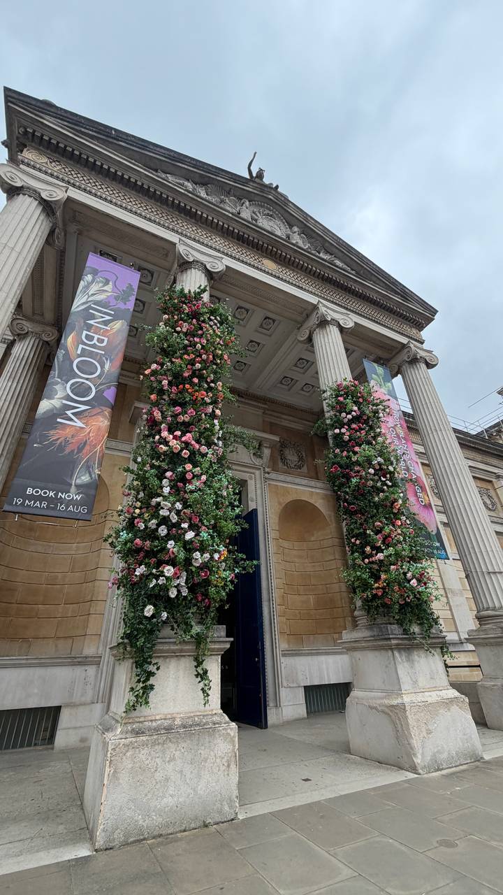 Grand museum entrance with neoclassical columns covered in vibrant floral displays and event banners.