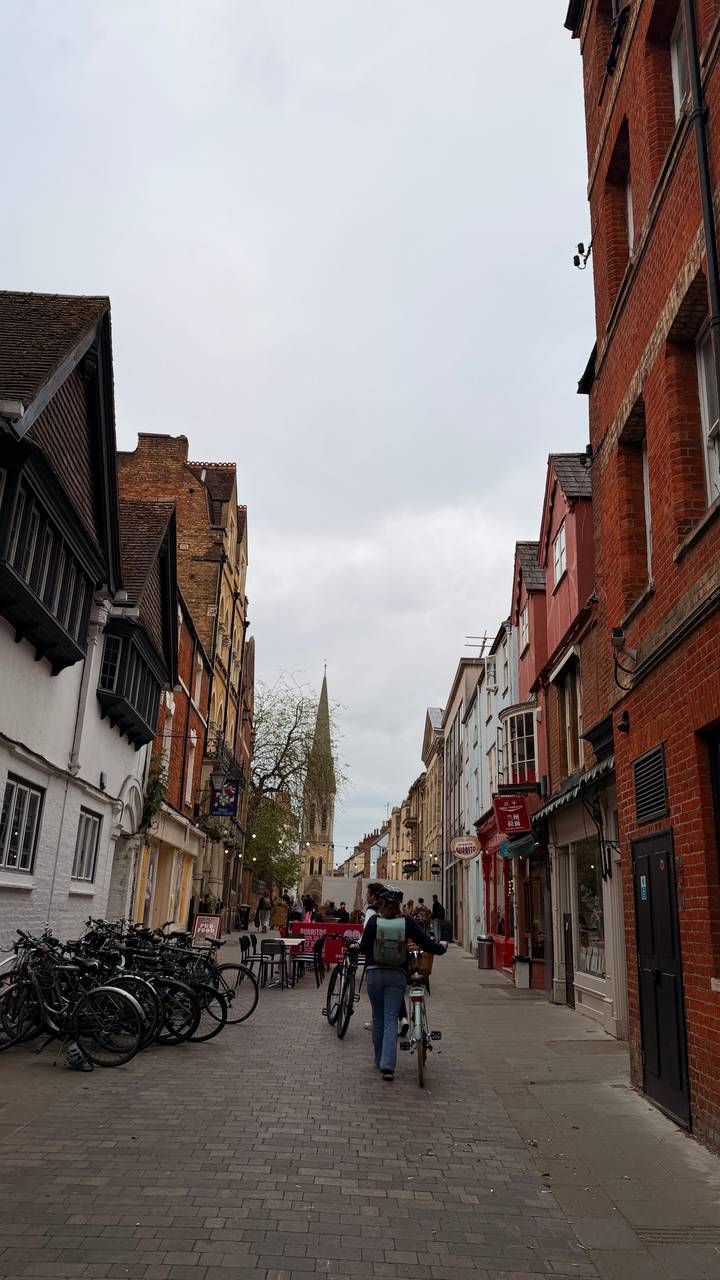 Historic brick and timber buildings line a narrow Oxford street that leads toward a distant church spire.