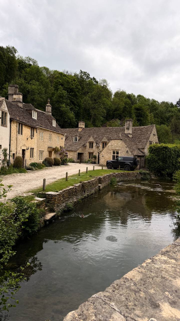 A tranquil scene of honey-coloured cottages and a stone bridge beside a reflective stream in a rural village.