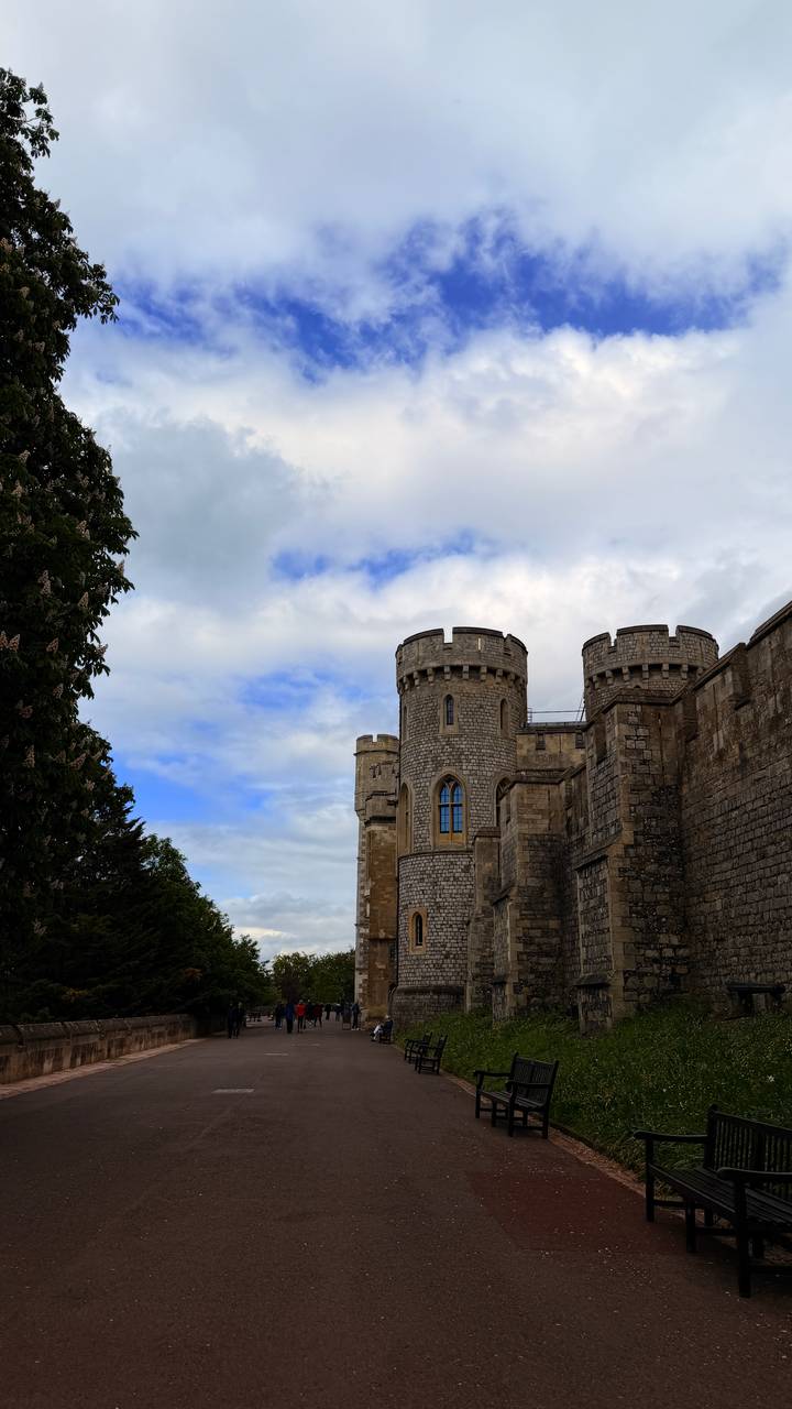 Stone towers of Windsor Castle rise against a partly cloudy blue sky.