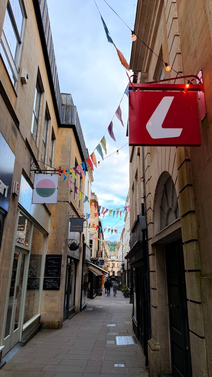 Colourful bunting and shop signs brighten a narrow pedestrian street between stone buildings.