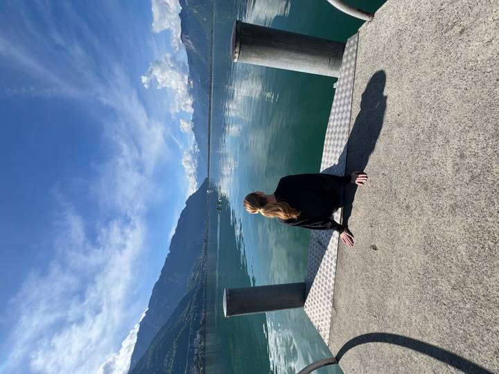 Young woman sitting on a dock gazing over a tranquil alpine lake with mountains mirrored in the water.