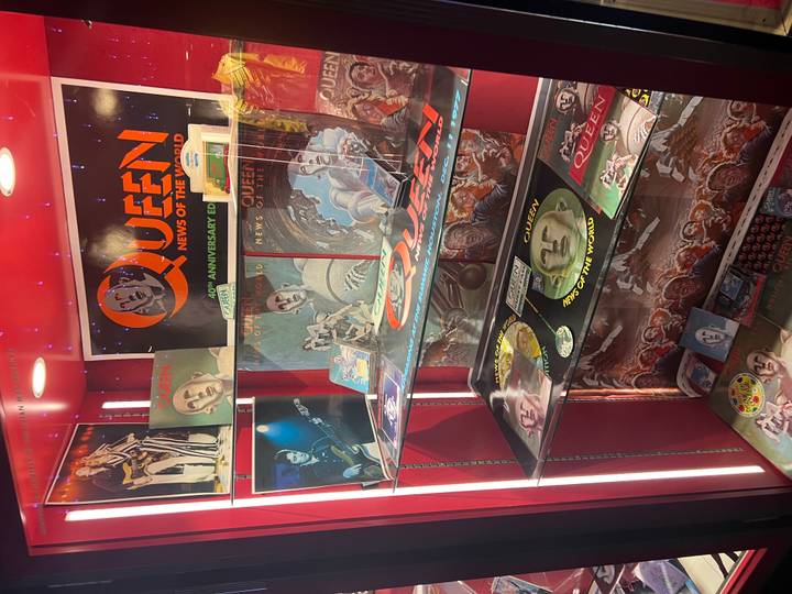 Museum-style display case filled with Queen band records and memorabilia under spotlights.