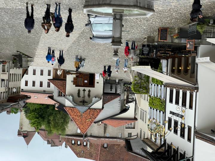 Cobblestoned village square with historic buildings and clusters of tourists strolling and dining outdoors.