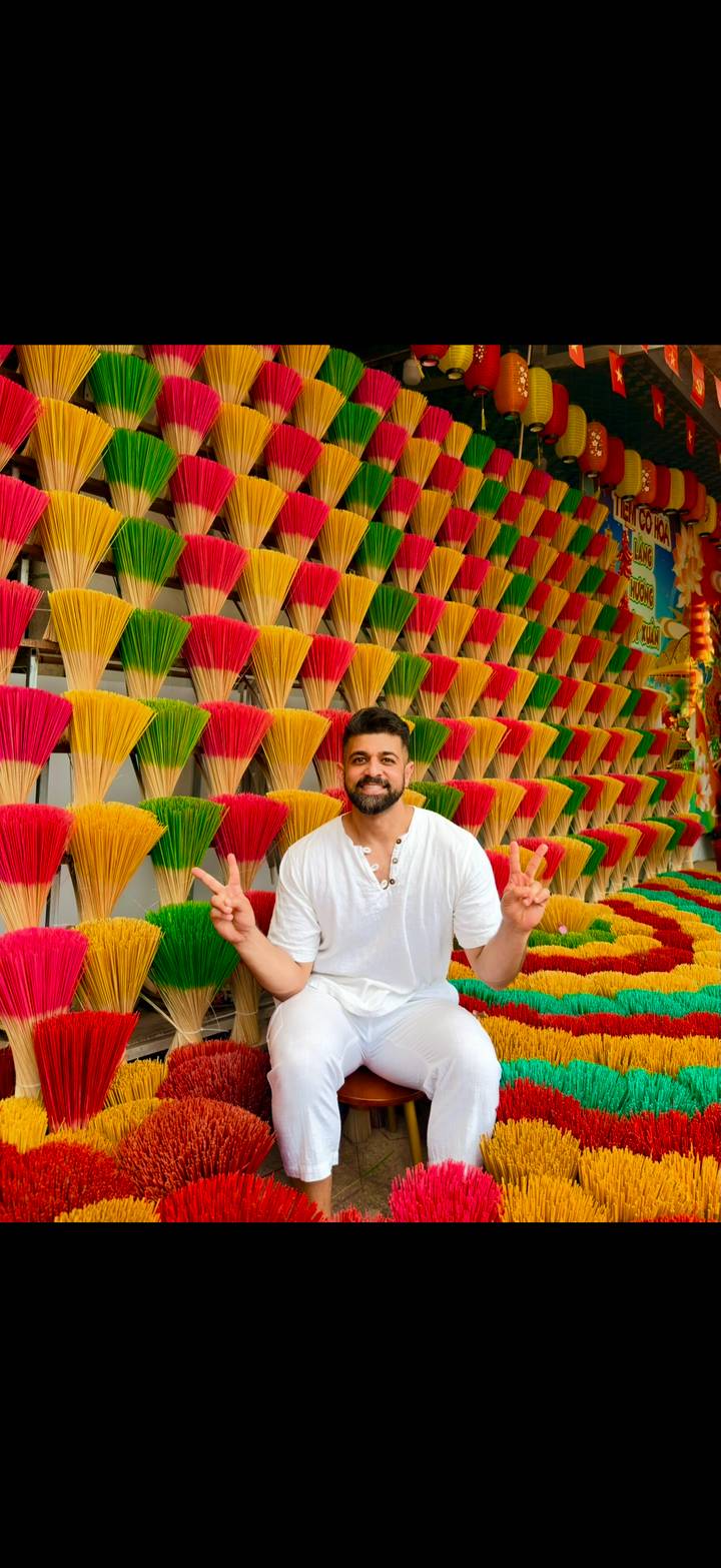 Traveller flashes peace signs in front of a vivid wall of multicoloured incense sticks.
